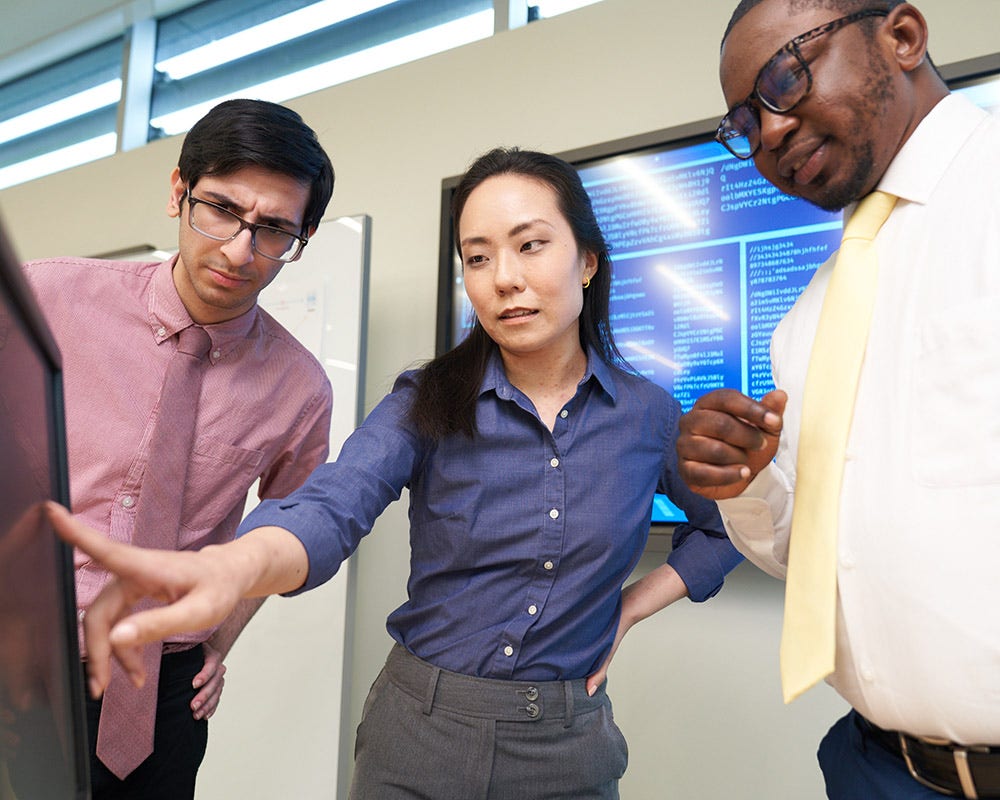 A UMGC bachelor's student, another person, and a UMGC bachelor's and master's student standing looking at a computer monitor.